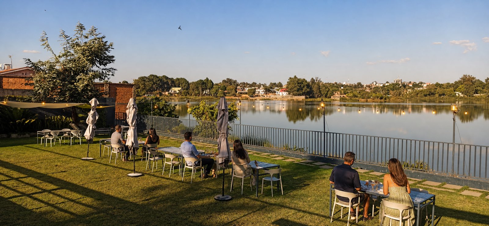 Pelouse de la résidence bordant le lac, tables et parasols en fin de journée